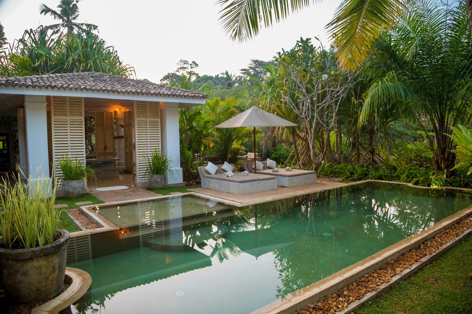Tiled-roof villa beside a garden pool surrounded by palms